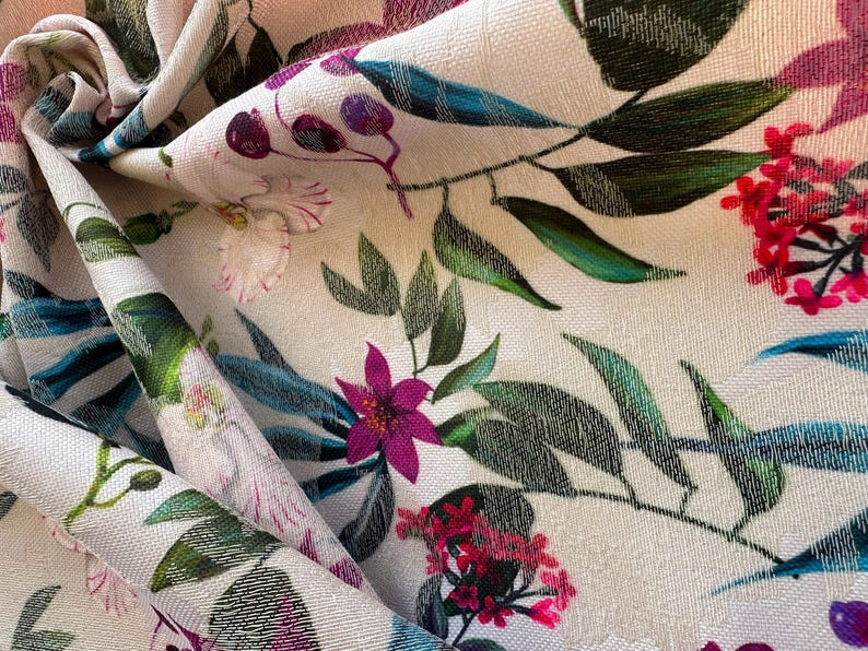 May include: A close-up of a white fabric with a floral print. The fabric features pink, purple, and green flowers on a white background.