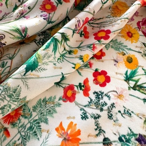 May include: White fabric with a floral print featuring red, orange, yellow, and green flowers. The fabric has a subtle gold glitter throughout.