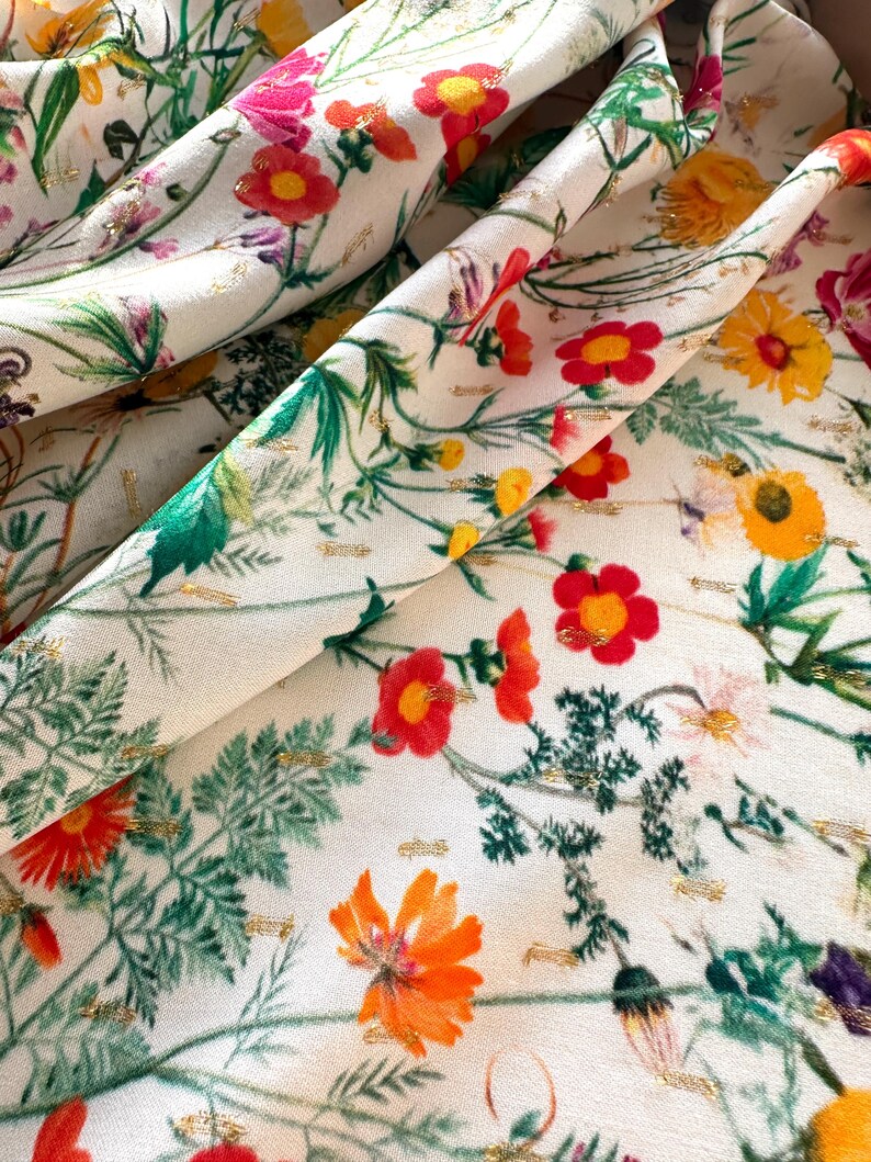 May include: White fabric with a floral print featuring red, orange, yellow, and green flowers. The fabric has a subtle gold glitter throughout.