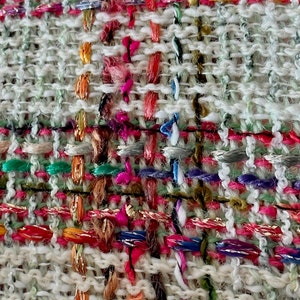 Puede incluir: Primer plano de una tela tejida con fondo blanco e hilos de colores. Los hilos est&aacute;n tejidos en un patr&oacute;n de cuadros, creando una superficie texturizada.