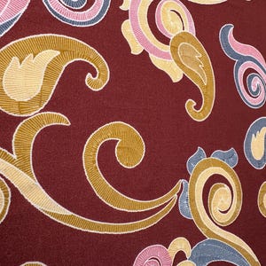 May include: A close-up of a burgundy fabric with a paisley pattern in shades of gold, pink, and blue.