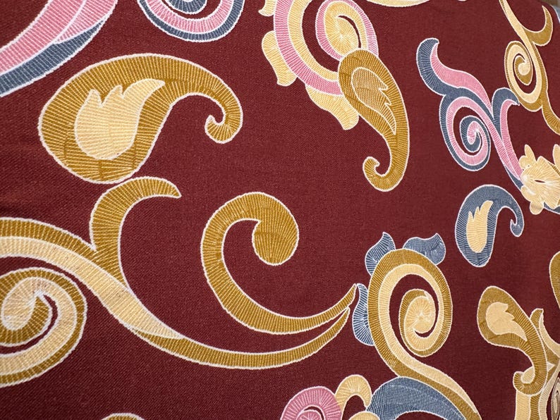 May include: A close-up of a burgundy fabric with a paisley pattern in shades of gold, pink, and blue.