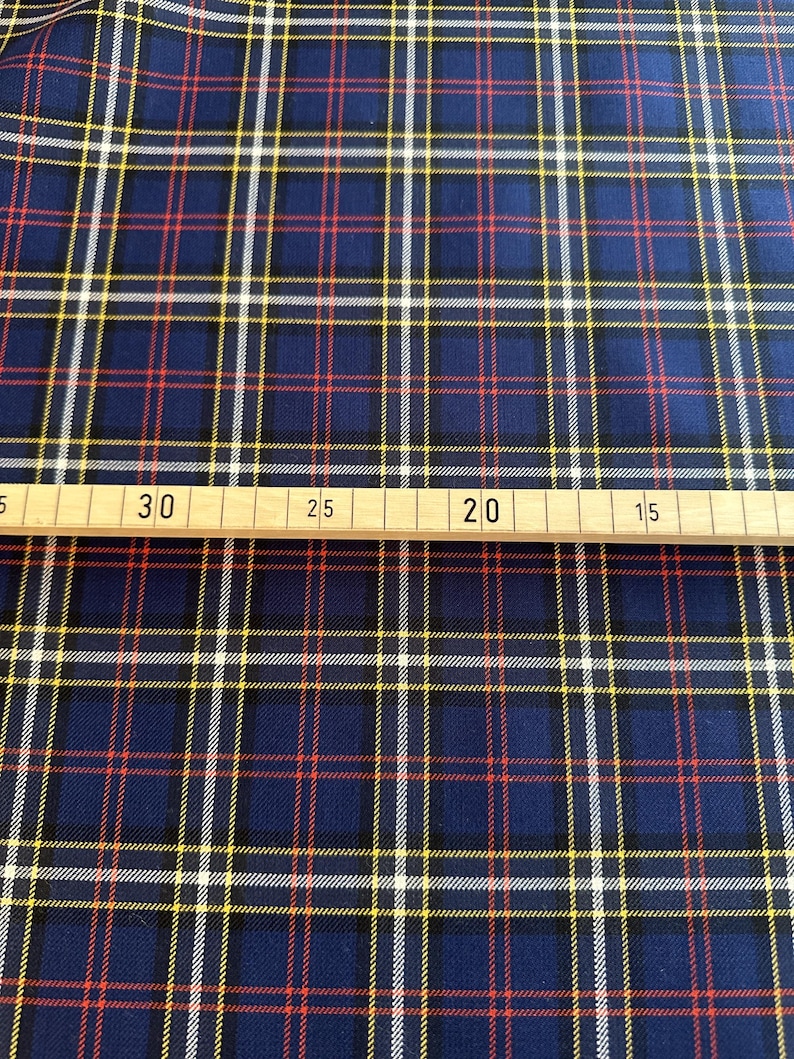 May include: Blue, red, white, and yellow plaid fabric. The fabric is measured with a ruler showing 30 inches.