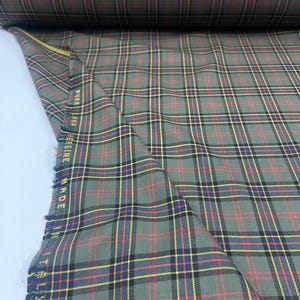 May include: Green, yellow, and red plaid fabric with a black stripe. The fabric is folded and the edge is visible. The text "PURE NEW WOOL MADE IN ITALY" is visible on the edge of the fabric.