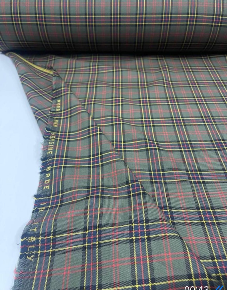 May include: Green, yellow, and red plaid fabric with a black stripe. The fabric is folded and the edge is visible. The text "PURE NEW WOOL MADE IN ITALY" is visible on the edge of the fabric.