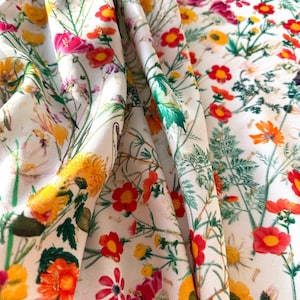 May include: White fabric with a floral print featuring red, yellow, and pink flowers with green leaves. The fabric has a subtle gold glitter throughout.