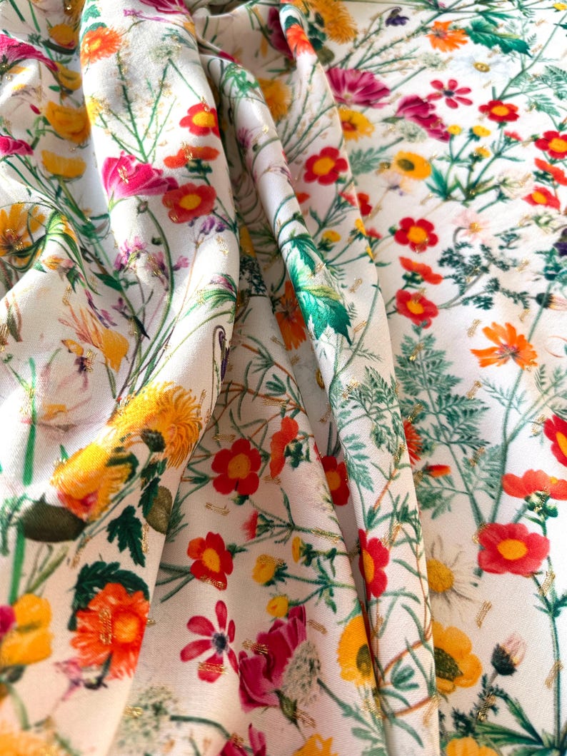 May include: White fabric with a floral print featuring red, yellow, and pink flowers with green leaves. The fabric has a subtle gold glitter throughout.