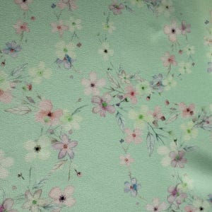 May include: A light green fabric with a delicate floral pattern. The flowers are in shades of pink, white, and blue.