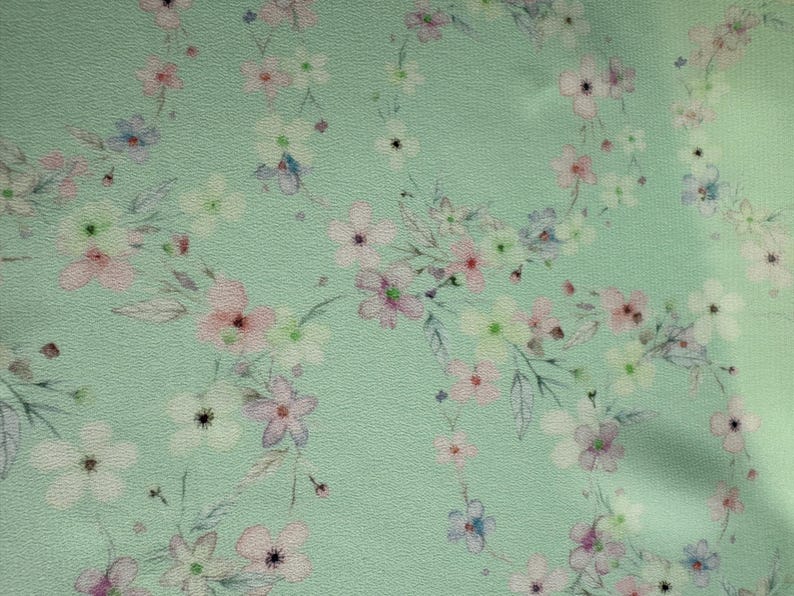 May include: A light green fabric with a delicate floral pattern. The flowers are in shades of pink, white, and blue.