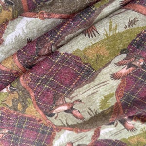 May include: Fabric with a repeating pattern featuring ducks in flight, plaid accents, and landscape elements in shades of burgundy, green, and tan. The fabric has a rustic, vintage aesthetic.