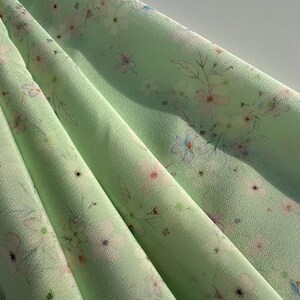 May include: A light green fabric with a delicate floral print. The fabric has a subtle sheen and a soft, flowing texture.