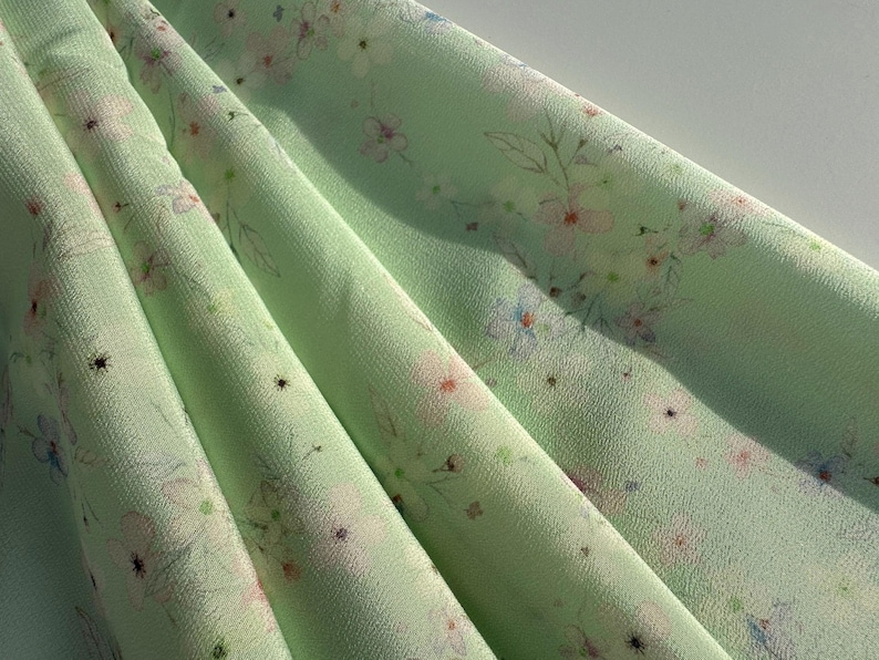 May include: A light green fabric with a delicate floral print. The fabric has a subtle sheen and a soft, flowing texture.
