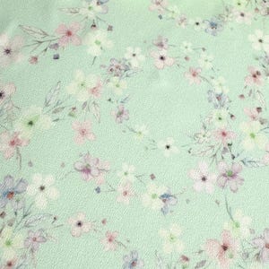 May include: A light green fabric with a delicate floral pattern. The flowers are in shades of pink, white, and blue.