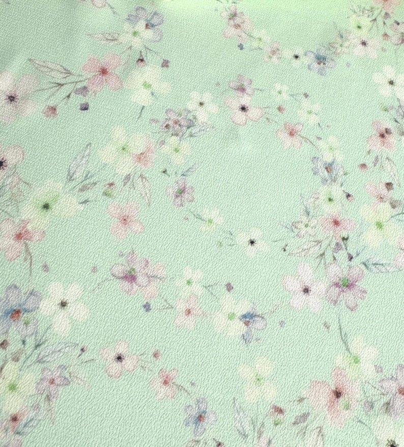 May include: A light green fabric with a delicate floral pattern. The flowers are in shades of pink, white, and blue.