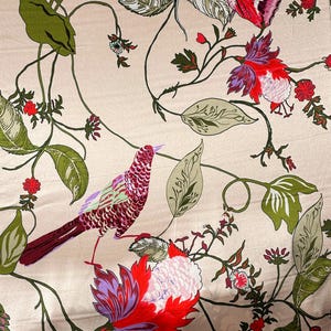 May include: A light beige fabric featuring a repeating pattern of birds, butterflies, and flowers. The design includes green leaves, red and purple blossoms, and a bird with red and purple plumage, all connected by thin, dark green winding vines.