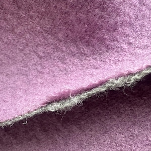 Peut inclure: Gros plan sur un tissu lavande texturé avec un bord gris. Le tissu semble doux et flou, avec des fibres visibles. Le bord est d'une couleur grise contrastante, créant une bordure visuelle. Ce textile pourrait être utilisé pour les vêtements ou la décoration intérieure.