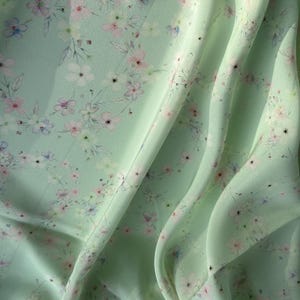 May include: A light green fabric with a delicate floral pattern. The fabric is soft and flowing, with a subtle sheen.