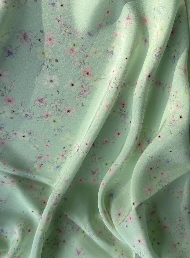 May include: A light green fabric with a delicate floral pattern. The fabric is soft and flowing, with a subtle sheen.