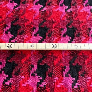 Puede incluir: Tela de pata de gallo roja, rosa y negra con textura tejida. La tela se mide con una regla que muestra 40, 35, 30 y 25.