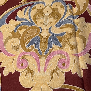 May include: A close-up of a burgundy fabric with a gold, pink, and blue damask pattern.