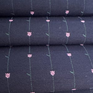 Könnte beinhalten: Nahaufnahme eines marineblauen Stoffes mit einem sich wiederholenden Muster aus rosa tulpenartigen Blumen und grünen Stielen. Der Stoff ist gefaltet und zeigt die Textur und das Design. Das Blumenmuster ist in vertikalen Reihen angeordnet.