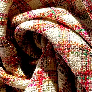 Puede incluir: Primer plano de una tela blanca con un estampado de cuadros de colores. La tela est&aacute; doblada y retorcida, creando un efecto de remolino.
