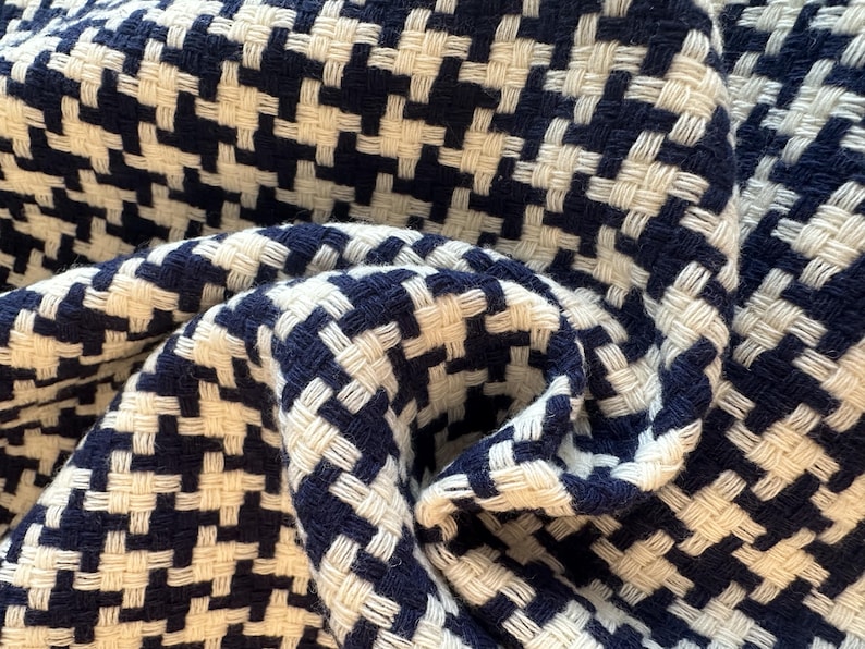 May include: Close-up of a woven fabric with a houndstooth pattern. The fabric features a repeating design of navy blue and off-white squares. The material is folded and draped, showing the texture and weave of the fabric.