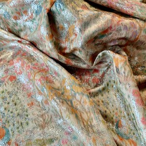 May include: Close-up of a metallic fabric with a floral pattern in shades of pink, orange, green, and silver.