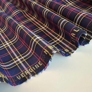 May include: Close-up of a blue, red, white, and yellow plaid fabric with a frayed edge.