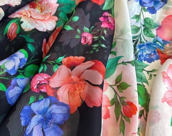 Pode incluir: Close-up de tecido floral em preto, branco e rosa. O tecido apresenta grandes flores coloridas em tons de vermelho, rosa e azul, com folhas verdes. As flores estão dispostas em um padrão repetitivo.