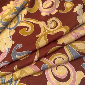 May include: Red fabric with a gold, pink, and blue paisley pattern. The fabric is folded in thirds.