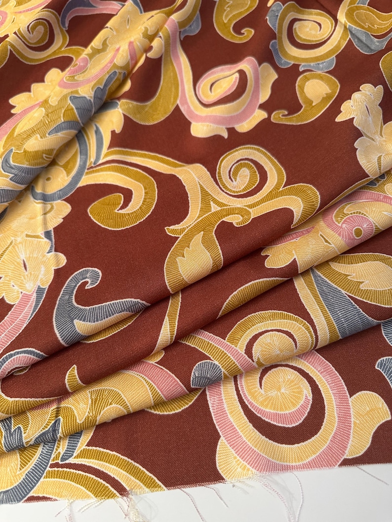 May include: Red fabric with a gold, pink, and blue paisley pattern. The fabric is folded in thirds.