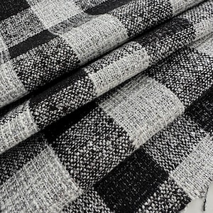 Puede incluir: Tela a cuadros en blanco y negro con un ligero brillo. La tela tiene una textura tejida y está doblada en varios lugares.