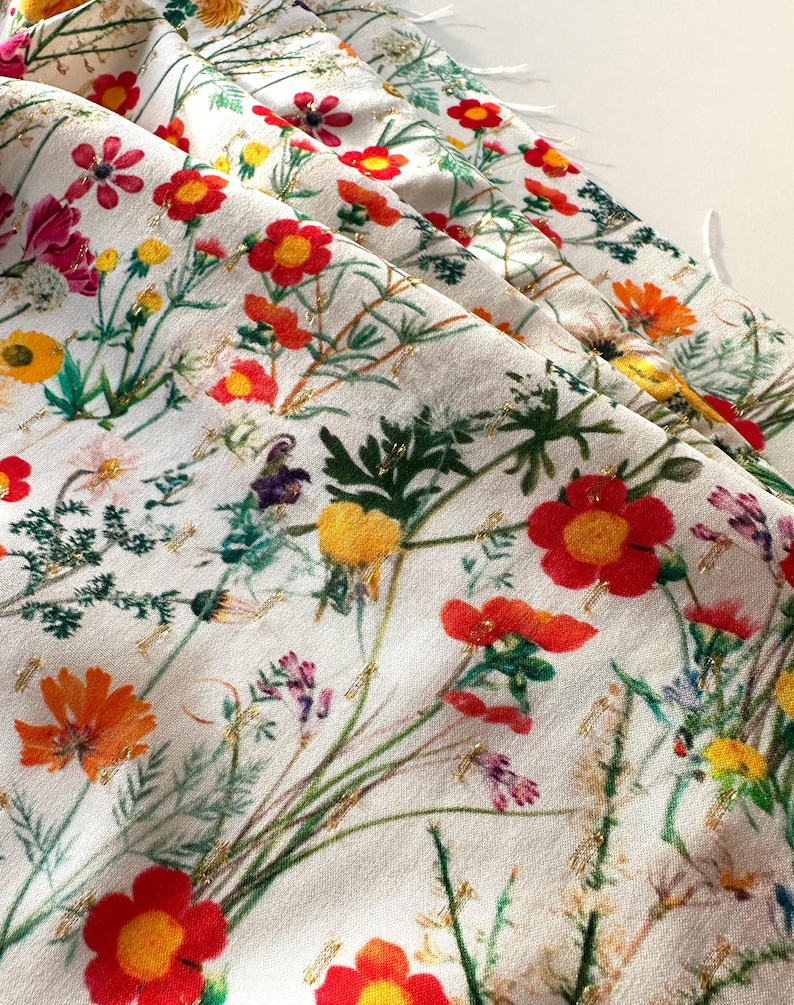 May include: White fabric with a floral print featuring red, yellow, and green flowers with gold accents.