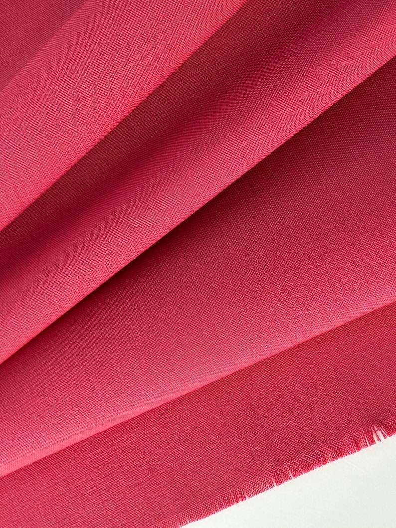 Op de afbeelding: Close-up van een gevouwen stuk rode stof met een licht ruwe textuur. De stof heeft een rauwe rand.