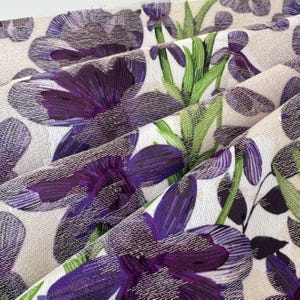 May include: Purple and green floral fabric with a textured surface. The fabric features a repeating pattern of flowers and leaves.