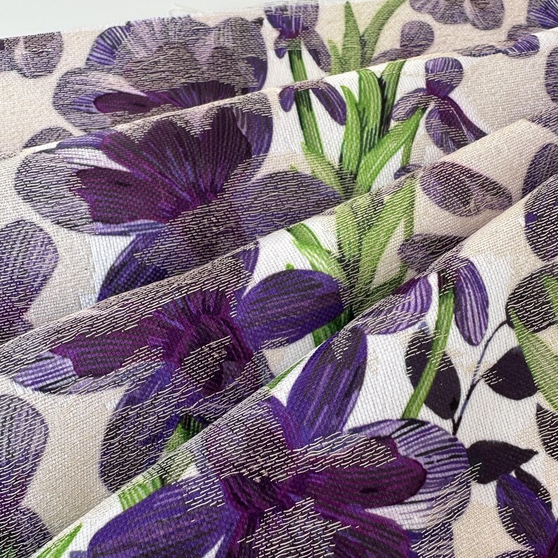 May include: Purple and green floral fabric with a textured surface. The fabric features a repeating pattern of flowers and leaves.