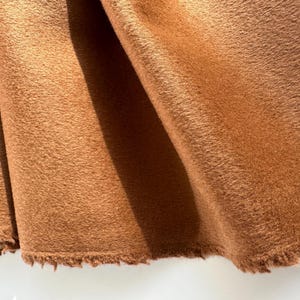 May include: Close-up of a section of brown fabric with a fuzzy texture. The fabric is folded, revealing the texture and the raw, unfinished edge. The color is a warm, earthy tone.