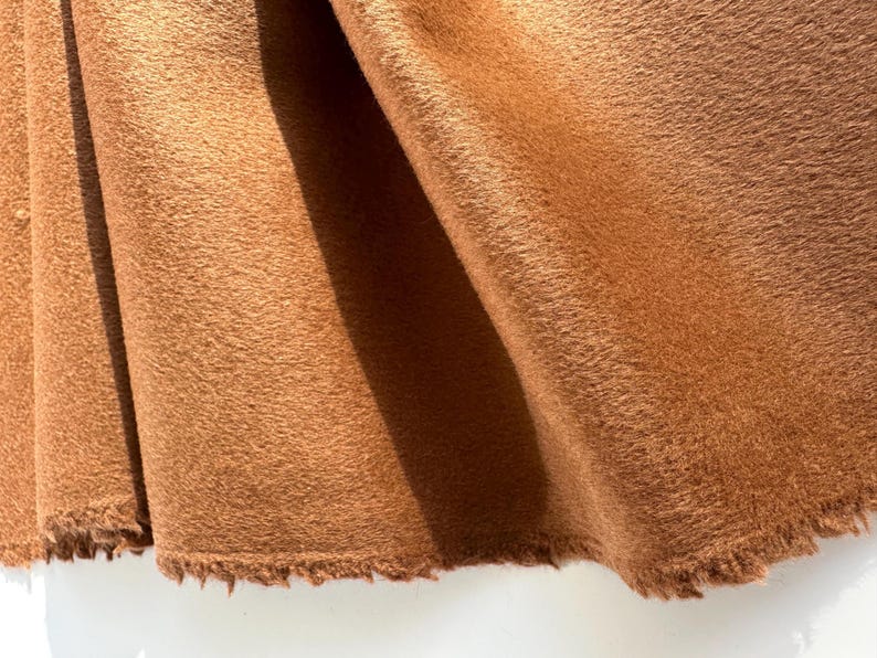 May include: Close-up of a section of brown fabric with a fuzzy texture. The fabric is folded, revealing the texture and the raw, unfinished edge. The color is a warm, earthy tone.