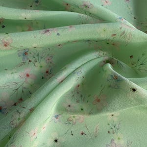 May include: A light green fabric with a delicate floral print. The fabric has a soft, flowing texture and is perfect for creating garments or home decor.