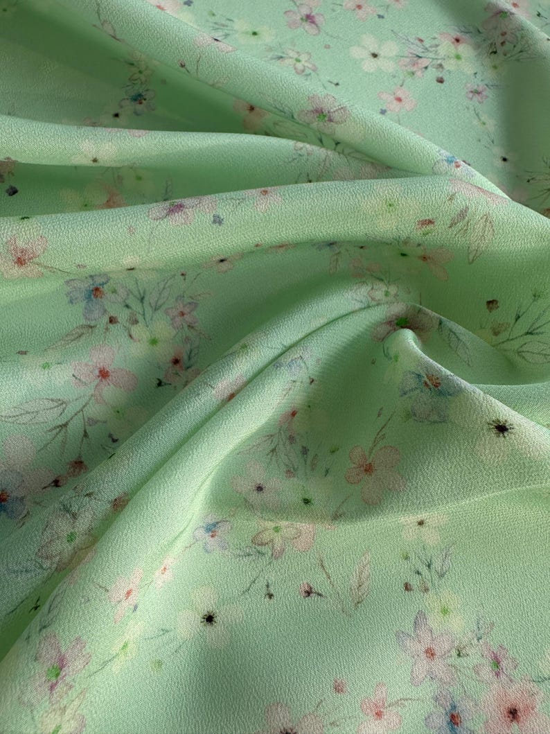 May include: A light green fabric with a delicate floral print. The fabric has a soft, flowing texture and is perfect for creating garments or home decor.