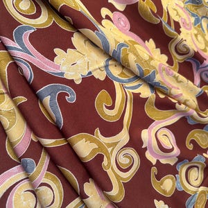 May include: A close-up of a fabric with a burgundy background and a swirling pattern in shades of gold, pink, and blue.