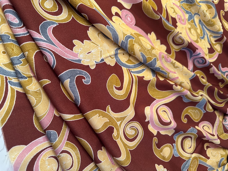 May include: A close-up of a fabric with a burgundy background and a swirling pattern in shades of gold, pink, and blue.