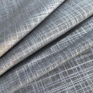 May include: Close-up of gray fabric with a subtle grid pattern. The fabric is folded, revealing layers and textures. The weave has a slightly textured appearance, with a mix of light and dark gray threads creating depth and visual interest. Ideal for apparel or home decor.