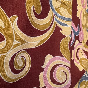 May include: A close-up of a fabric with a burgundy background and a swirling pattern of gold, pink, and blue.