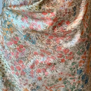 May include: Close-up of a fabric with a cream background and a colorful, abstract pattern. The fabric has a metallic sheen and a slightly textured surface.