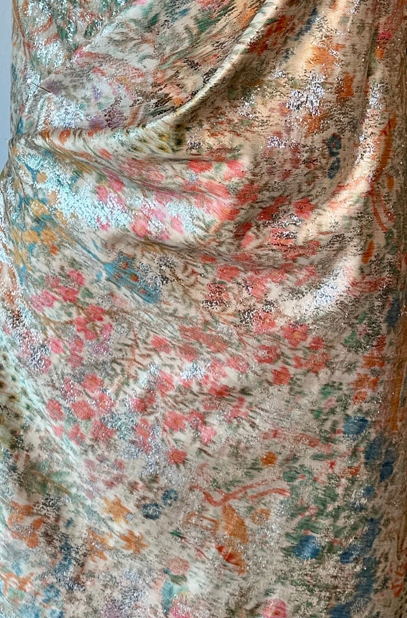 May include: Close-up of a fabric with a cream background and a colorful, abstract pattern. The fabric has a metallic sheen and a slightly textured surface.