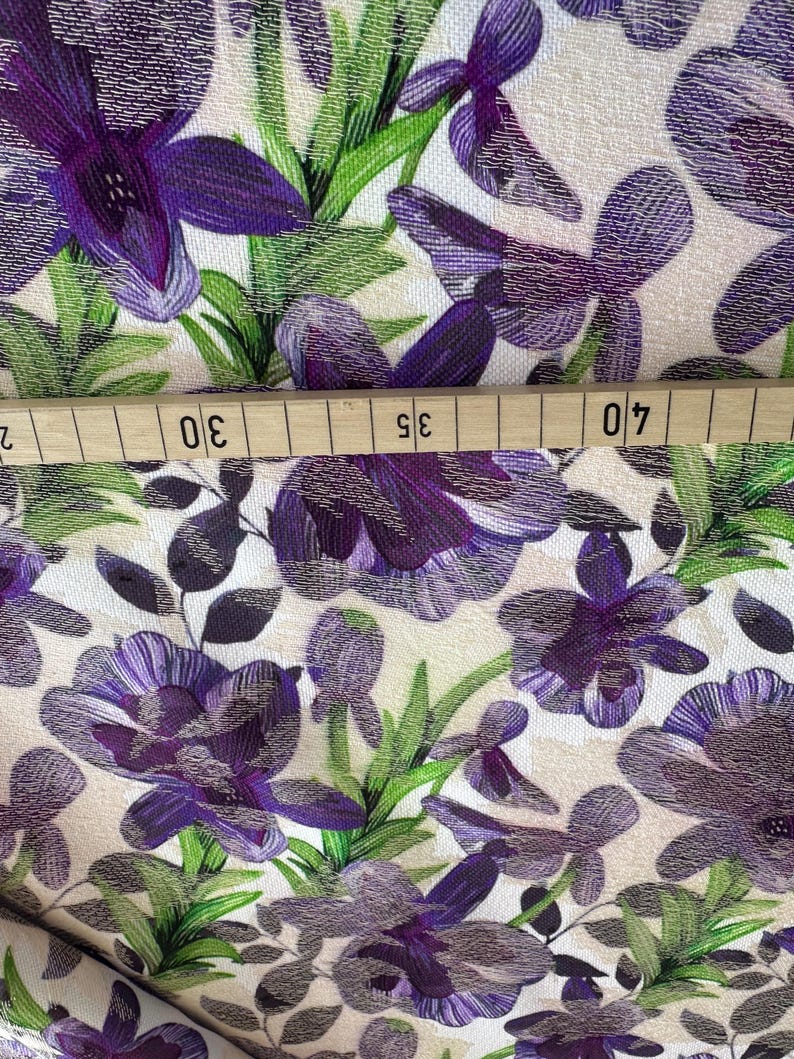 May include: Purple and green floral fabric with a white background. The fabric has a textured surface and a repeating pattern of flowers and leaves.