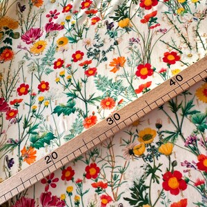 May include: A white fabric with a floral print featuring red, yellow, and orange flowers. A wooden ruler with markings in inches is placed on top of the fabric. The ruler shows measurements from 20 to 40 inches.