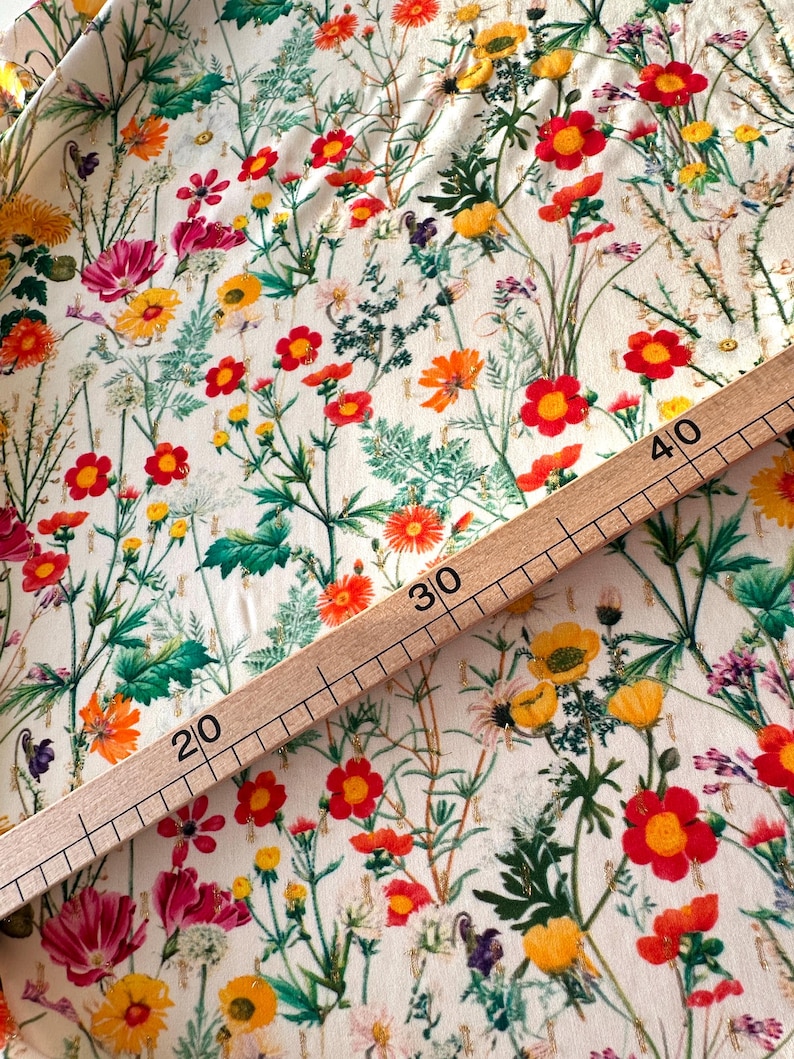 May include: A white fabric with a floral print featuring red, yellow, and orange flowers. A wooden ruler with markings in inches is placed on top of the fabric. The ruler shows measurements from 20 to 40 inches.